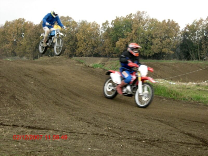 two boys riding a Honda HM 50 cc and a Fantic Motor Caballero 50 cc, 1975, in a motocross track while jumping, in daylight.