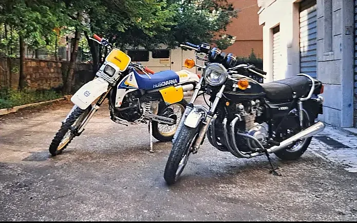 Vintage enduro 1988 Husqvarna TE 510 and classic 1980 Kawasaki Z 1000 parked in the garden front three-quarter shot, sunny day.