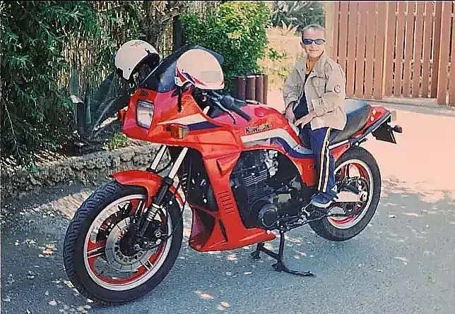 A Kawasaki GPZ 1100 cc Unitrack red colour, with a kid on the saddle, front three-quarter shot.
