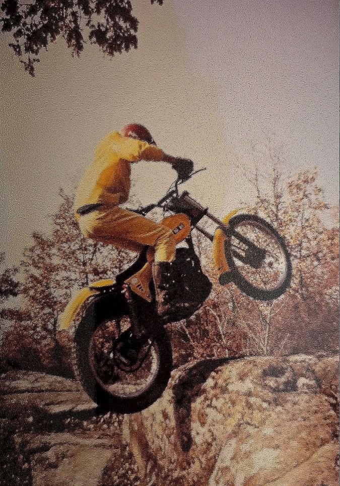 The rider is climbing a square stone in the countryside with his motorcycle SWM 320 trial.