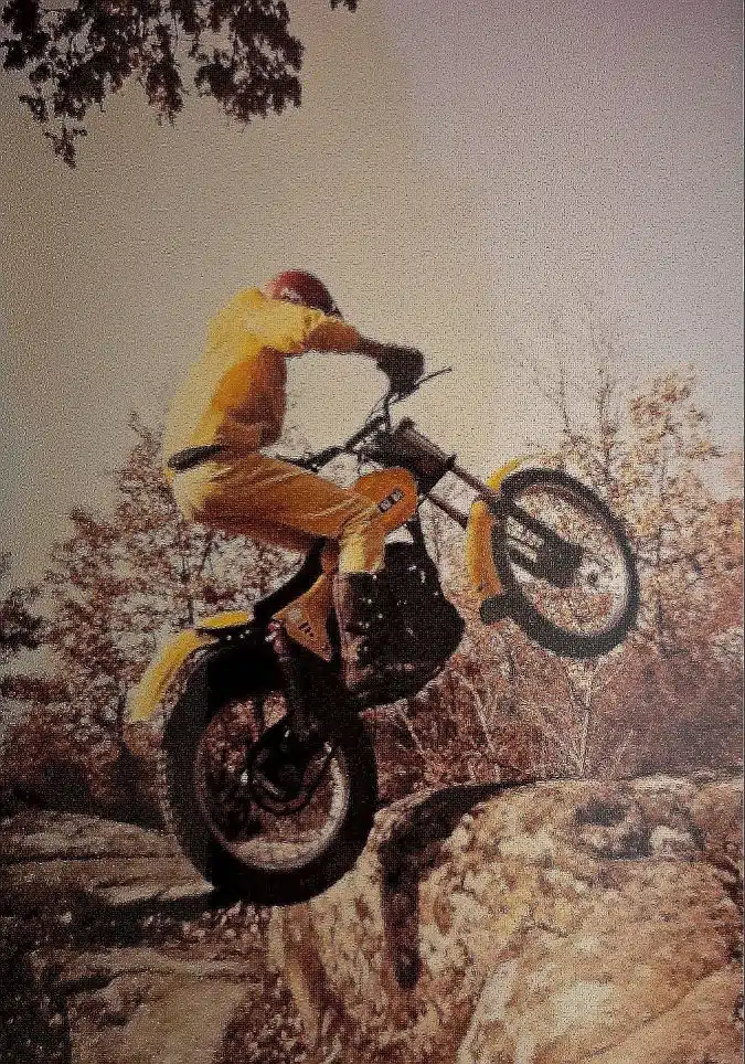 The rider is climbing a square stone in the countryside with his motorcycle SWM 320 trial.